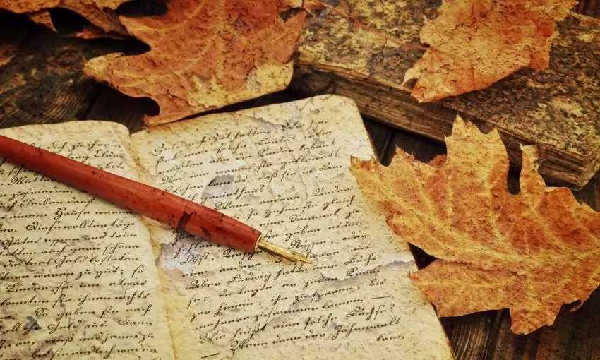 Plume et cahiers anciens entourés de feuilles mortes, pour écrire un conte de fée ou des légendes traditionnelles.