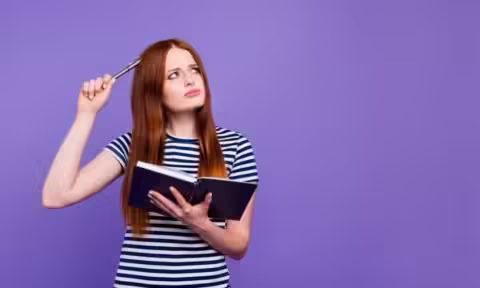 Une jeune femme tient un livre et un stylo, les yeux tournés vers le ciel, elle va lutter contre le syndrome de la page blanche grâce à Alchimie du Verbe.